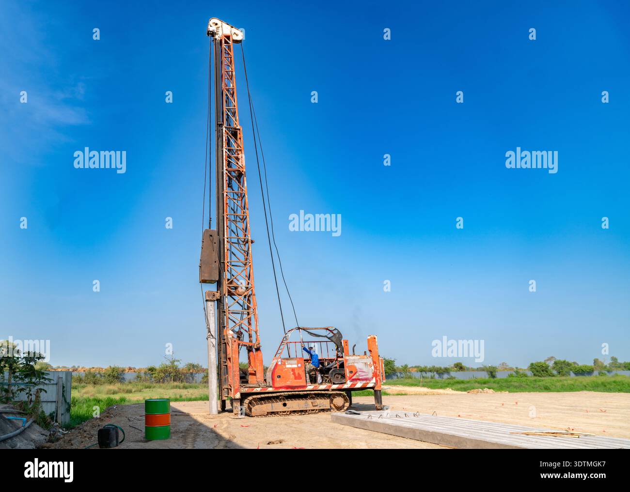 A tall hydraulic crawler piling rig stands against a clear blue sky ...