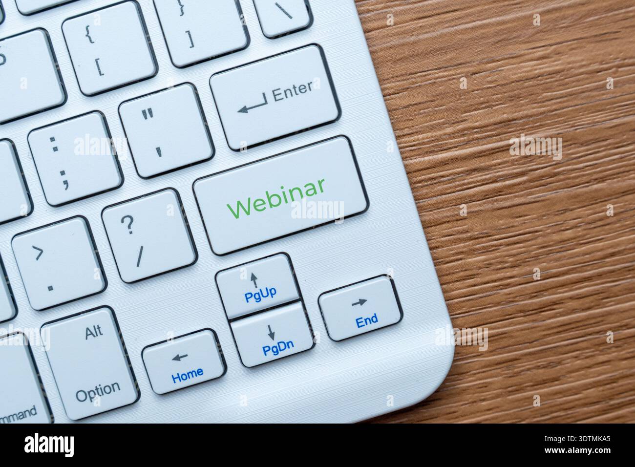 A computer keyboard on a wooden desk with a green Webinar key. Online education, virtual seminars, remote work concept. Copy space for text. Stock Photo
