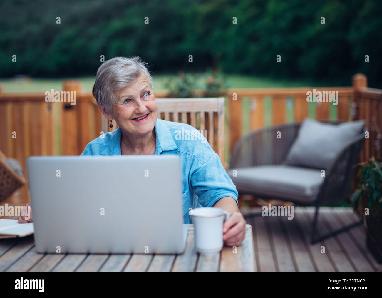 Mature woman sitting on balcony with laptop, working remotely. Stock Photo