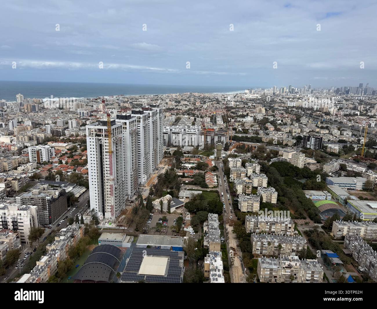 High-angle urban landscape showing modern white skyscrapers and residential buildings in a coastal city, with the blue ocean visible on the horizon. - Smartphone Captured Stock Image