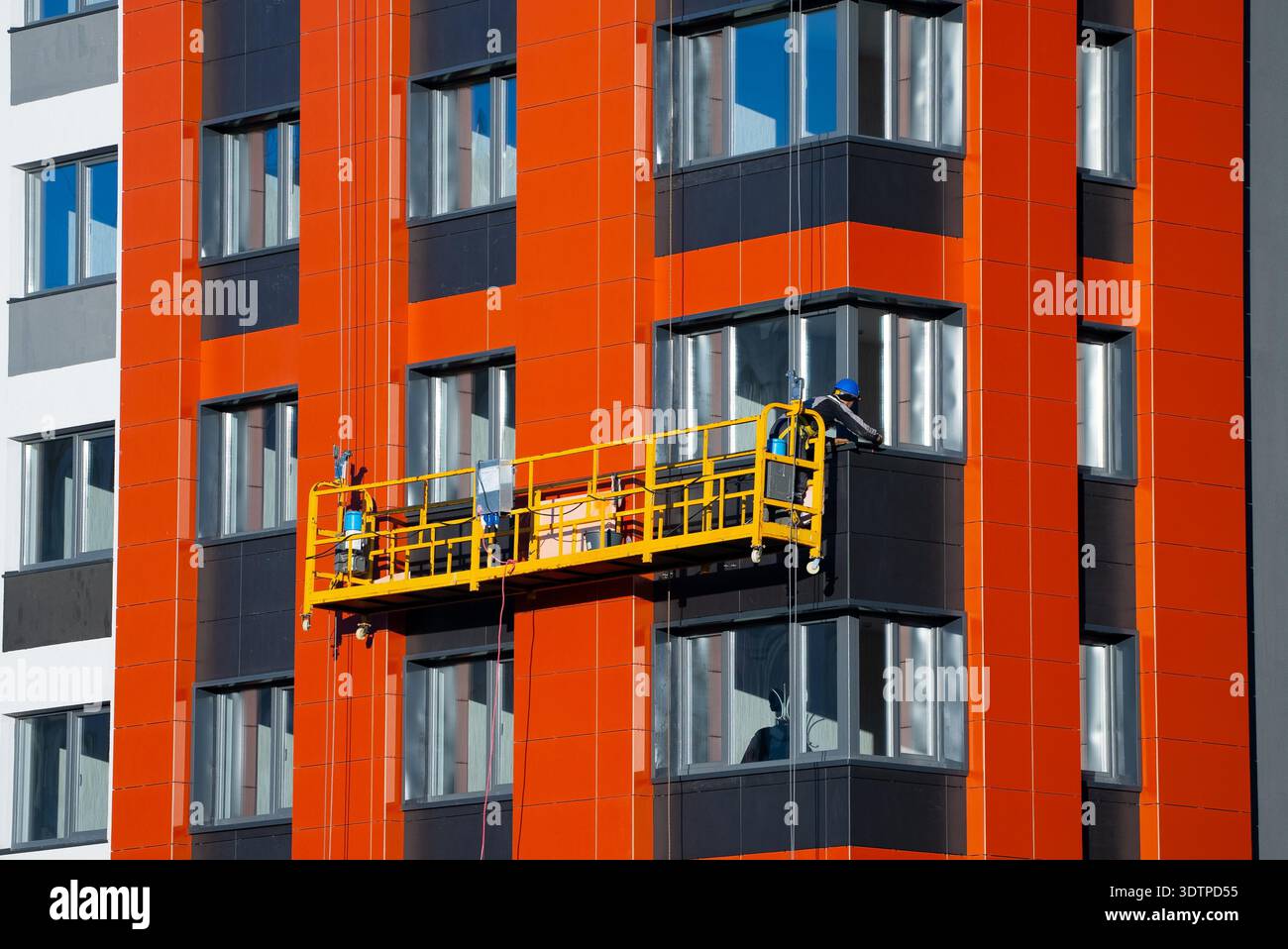 Construction worker on a suspended platform installs facade panels on a ...