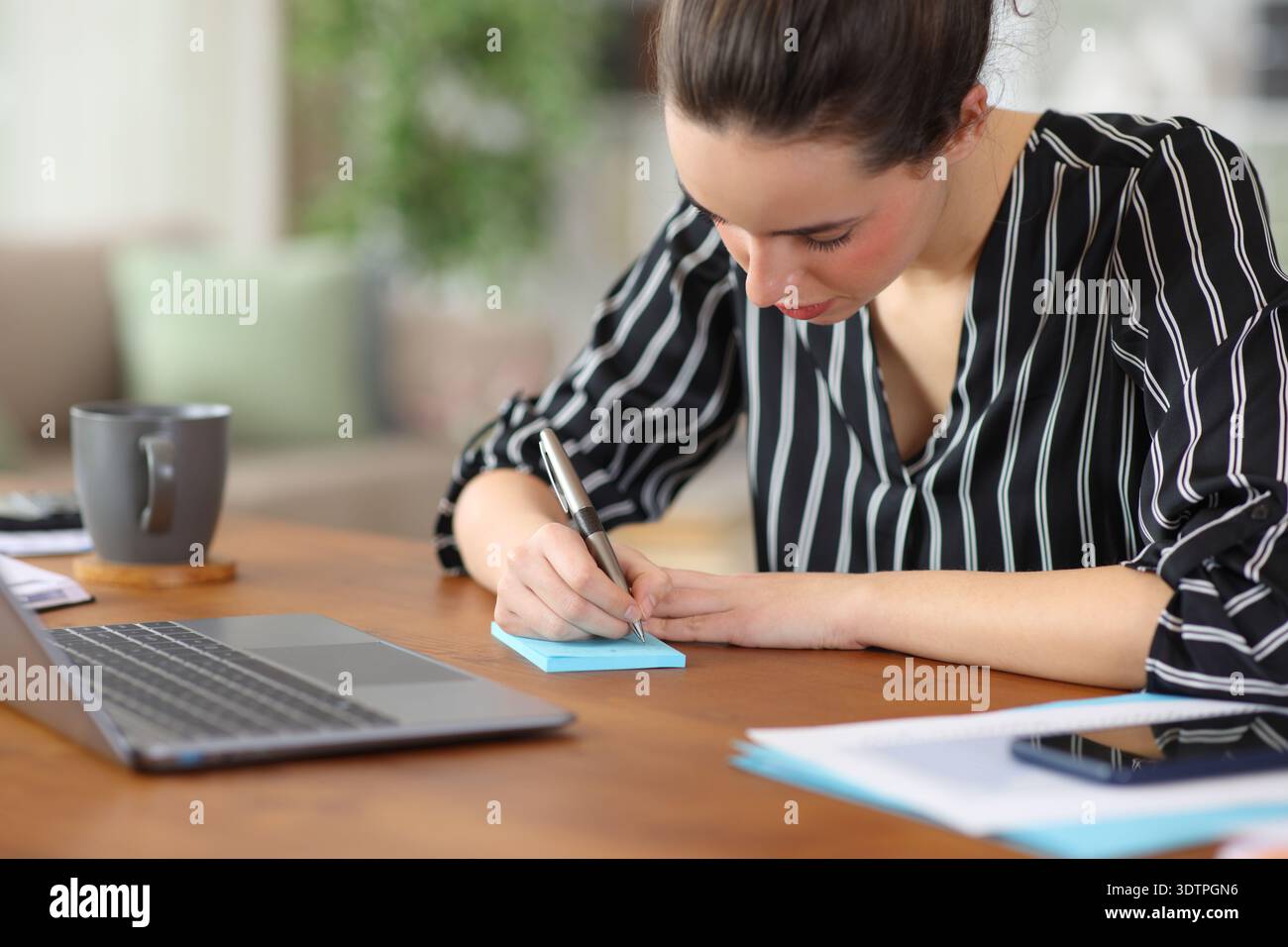 Freelance worker writing in blue sticky note in a desk working at home Stock Photo