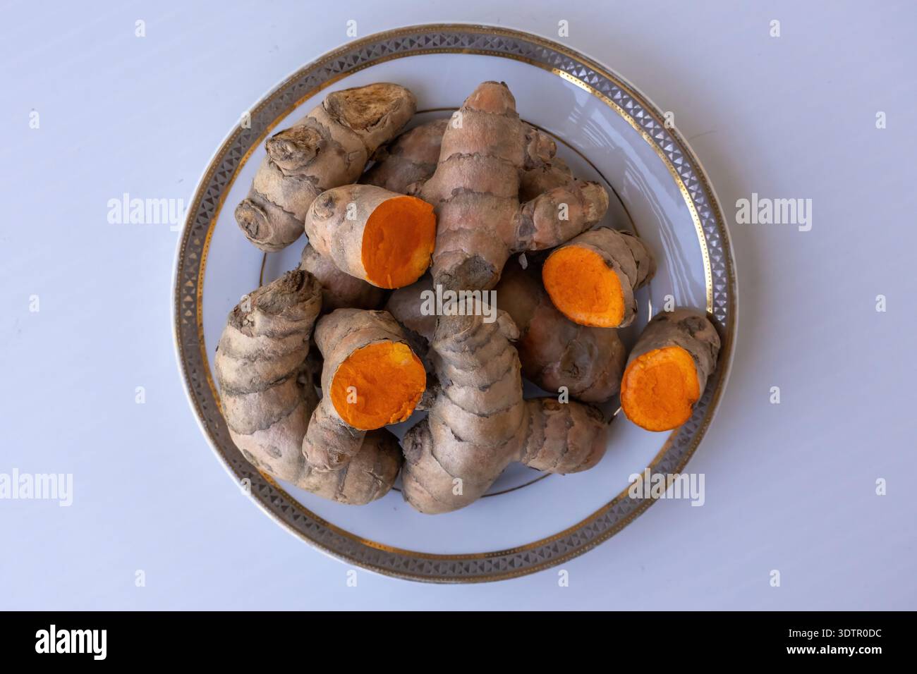 Top view of fresh raw turmeric (Curcuma longa) roots and slices on a white plate. Organic rhizomes showing bright orange inside. Isolated on white bac Stock Photo