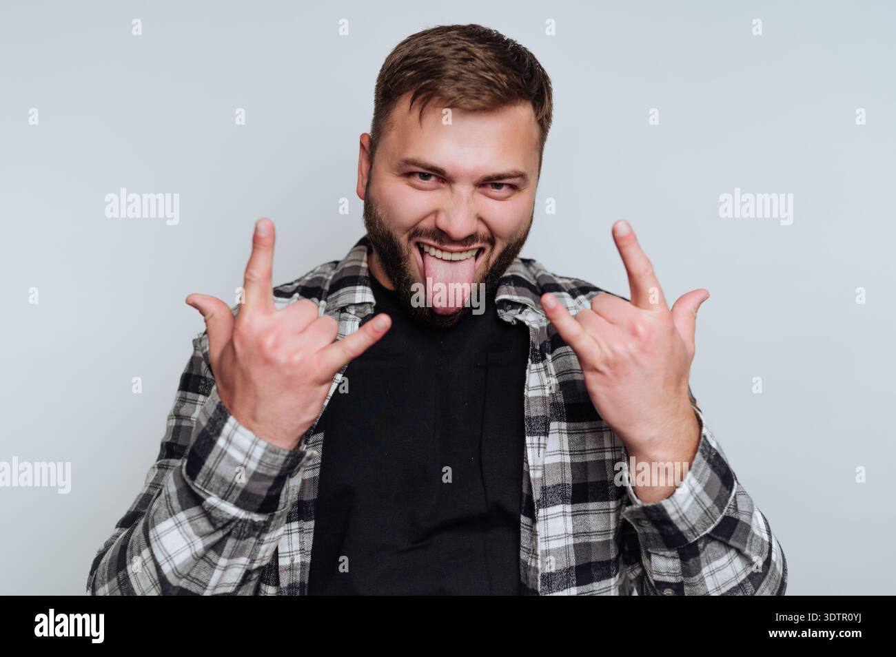 A young man stands confidently in a simple studio with a bright background. Stock Photo