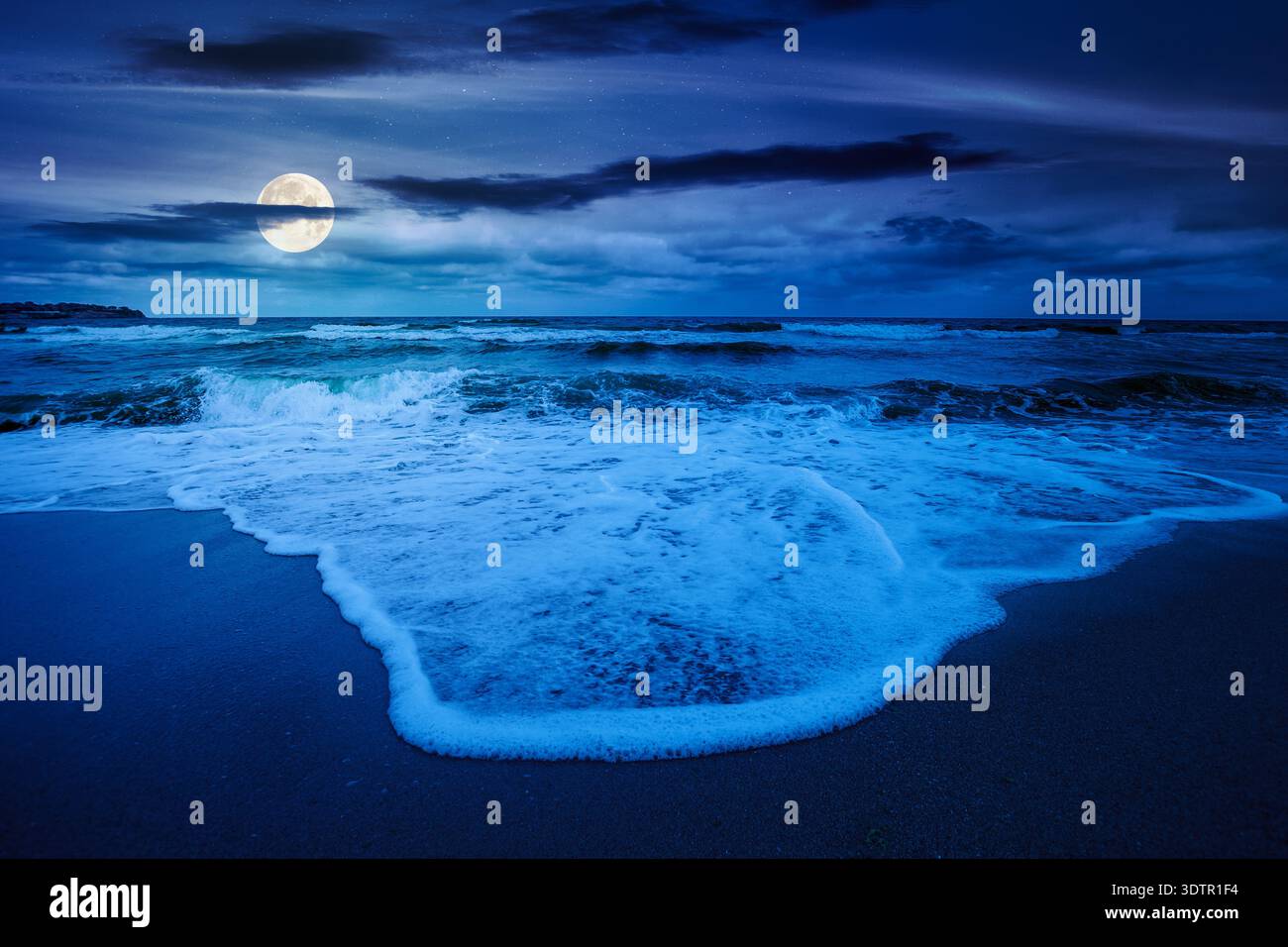 tide rolling on the sandy beach at night. full moon over sea waves beneath a cloudy sky. empty calm scenery in summer. loneliness concept. mysterious Stock Photo