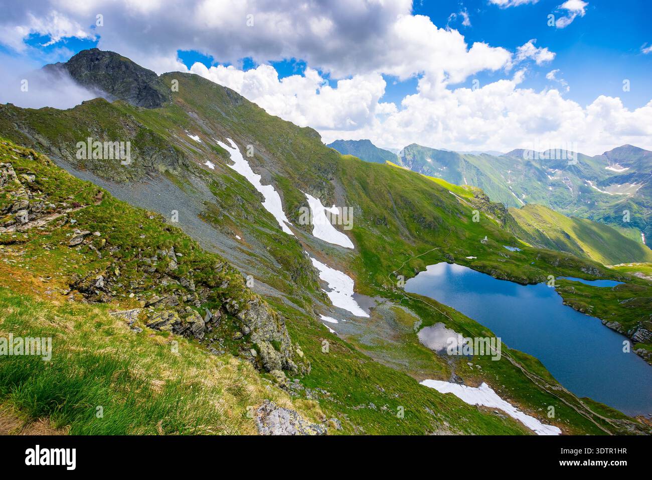 mountain lake in alpine summer landscape. beautiful view surrounded with transylvania alps and clouds on a blue sky. fresh water, snow and rocky slope Stock Photo