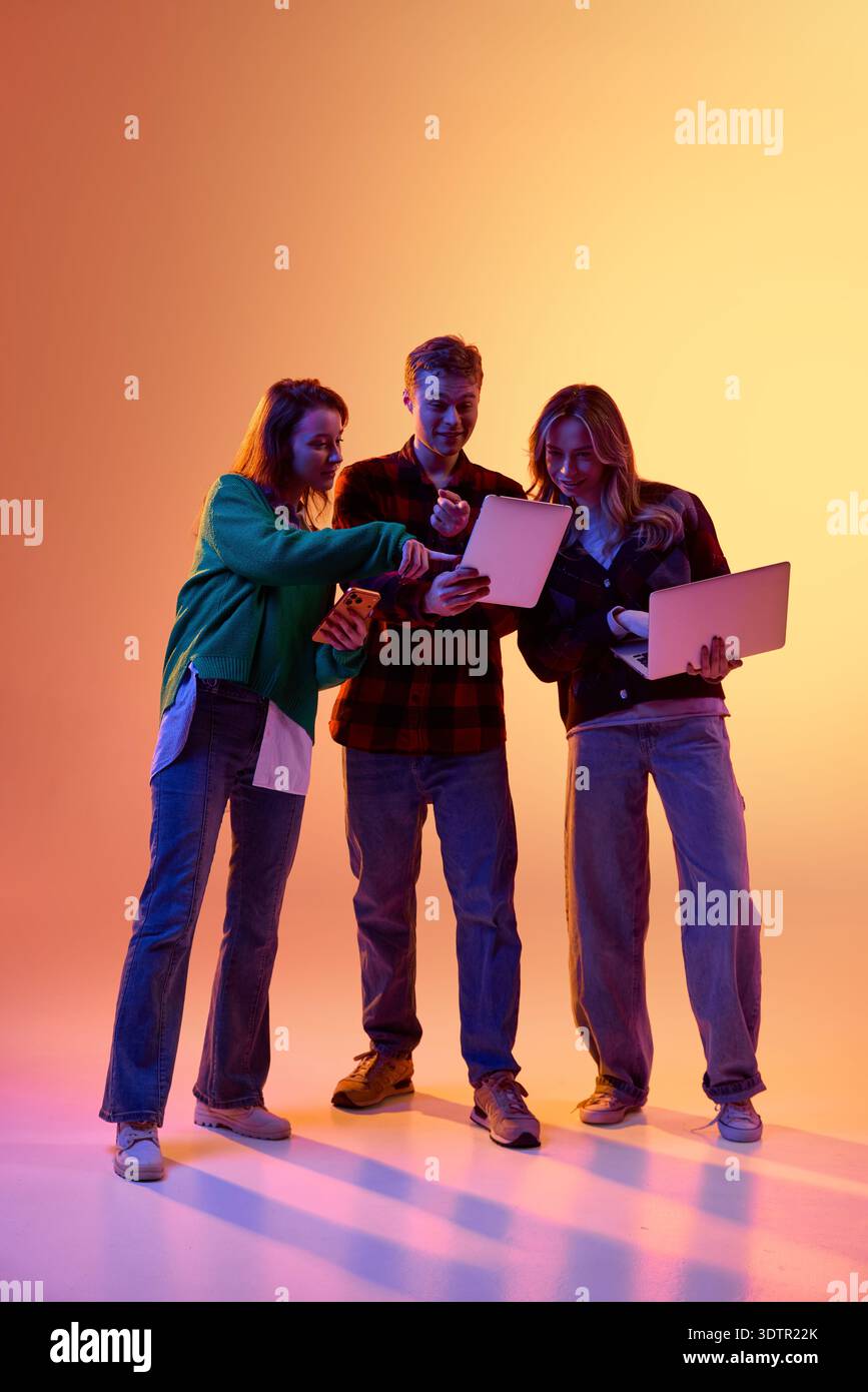 Three young professionals using tablet smartphone and laptop on gradient background Stock Photo
