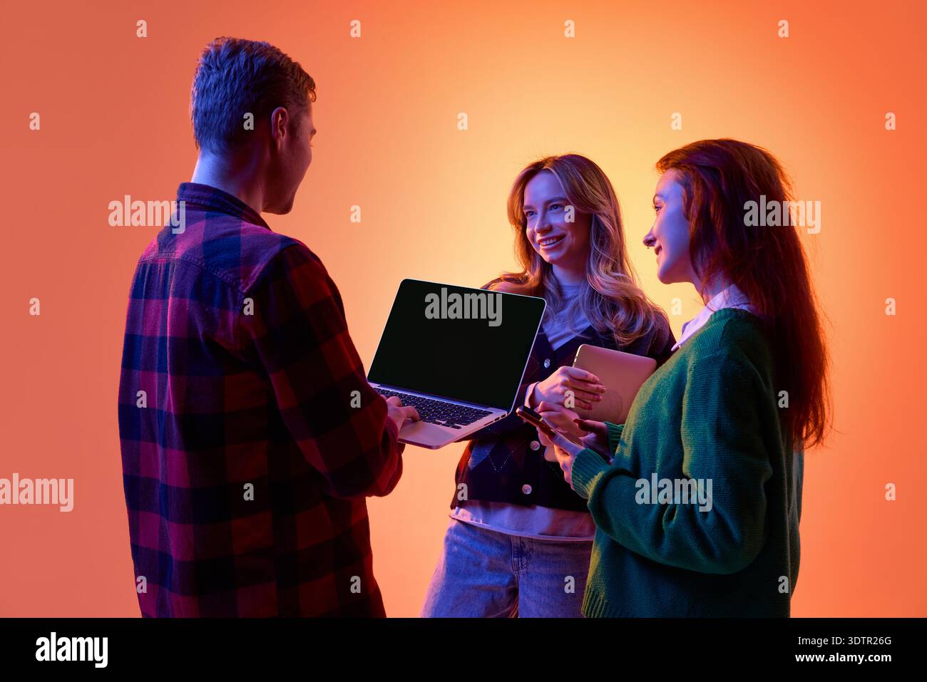 Three young professionals discussing project using laptop and tablet on gradient background. Stock Photo