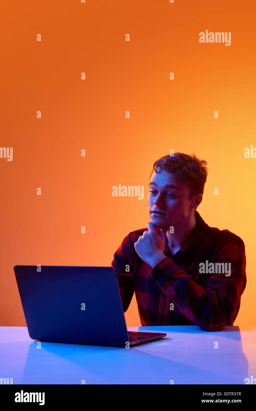 Young professional analyzing data on laptop against gradient background. Stock Photo