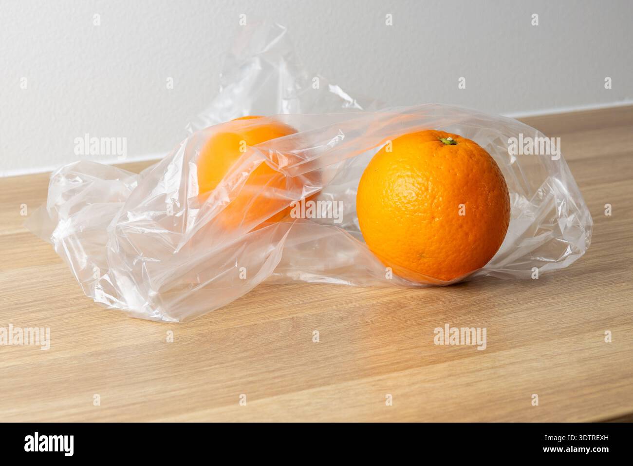 Two oranges wrapped in plastic on a wooden table, showcasing a simple, everyday scene. Stock Photo