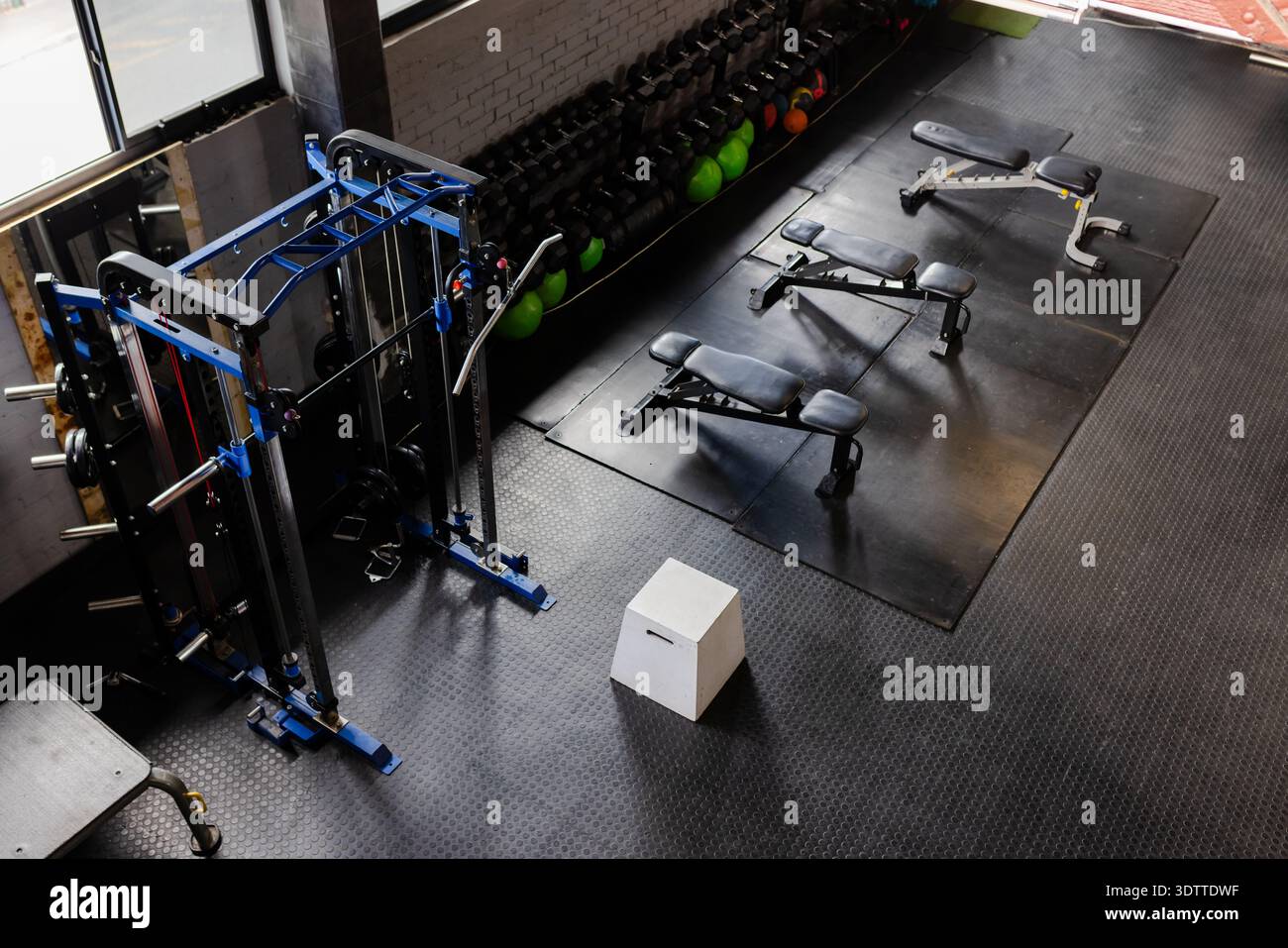 White plyometric box is sitting on black rubber floor near blue cable machine and benches Stock Photo