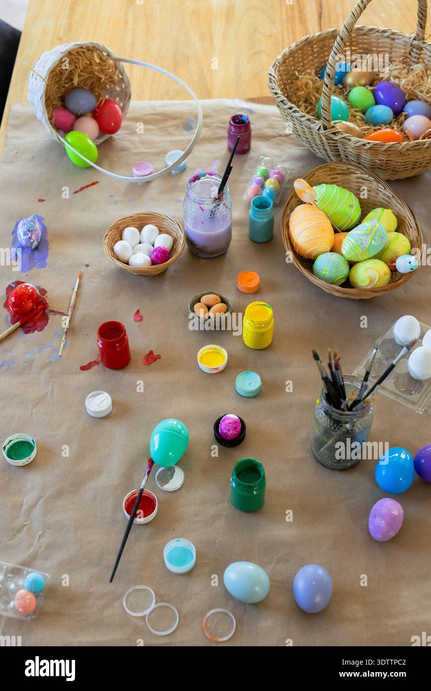 Painted and unpainted eggs are drying and spilling on wooden craft table, paint jars and brushes Stock Photo