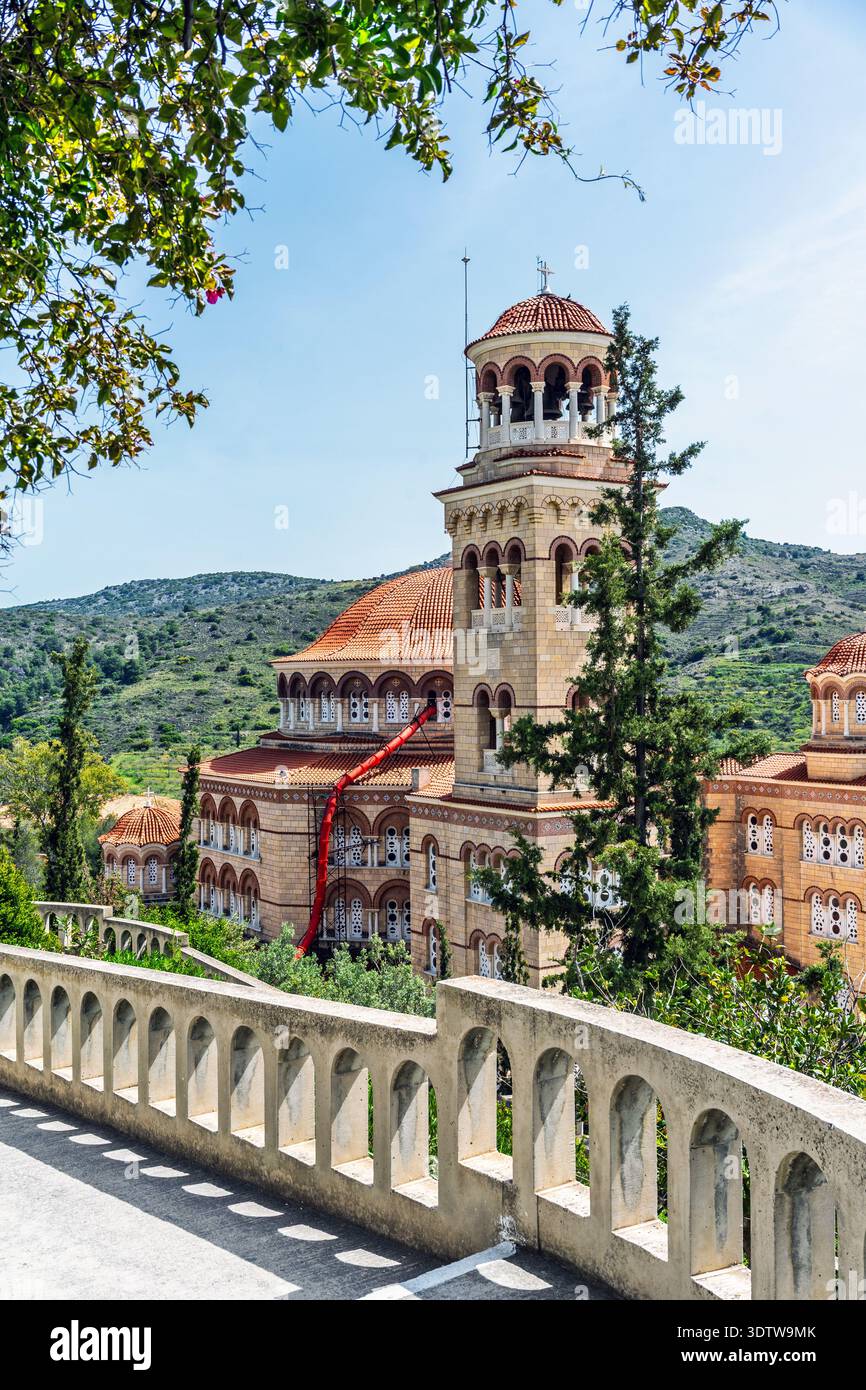 Agios Nektarios Monastery in Aegina, Greece, with its bell tower and red tiled domes rising above lush hills, framed by trees Stock Photo