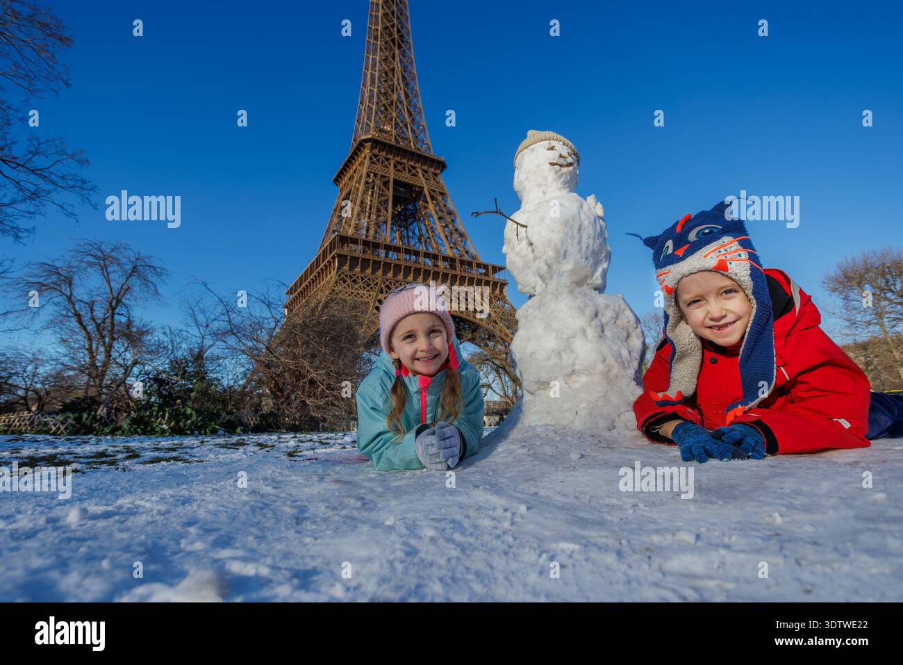 Two children are joyfully building a snowman in front of the Eiffel ...