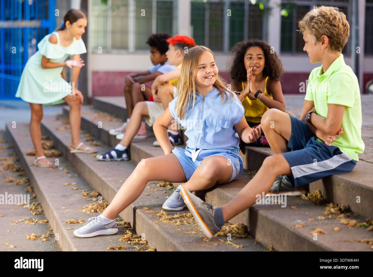 Happy tweenagers friends sitting on steps outdoors and chatting Stock Photo