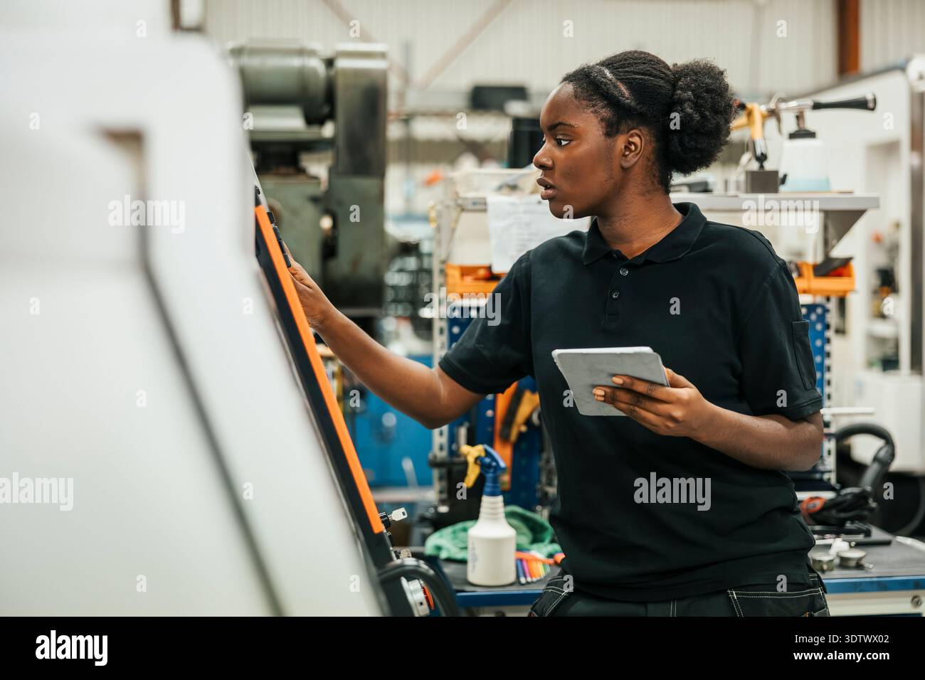 Young female worker holding tablet PC operating machine in factory Stock Photo