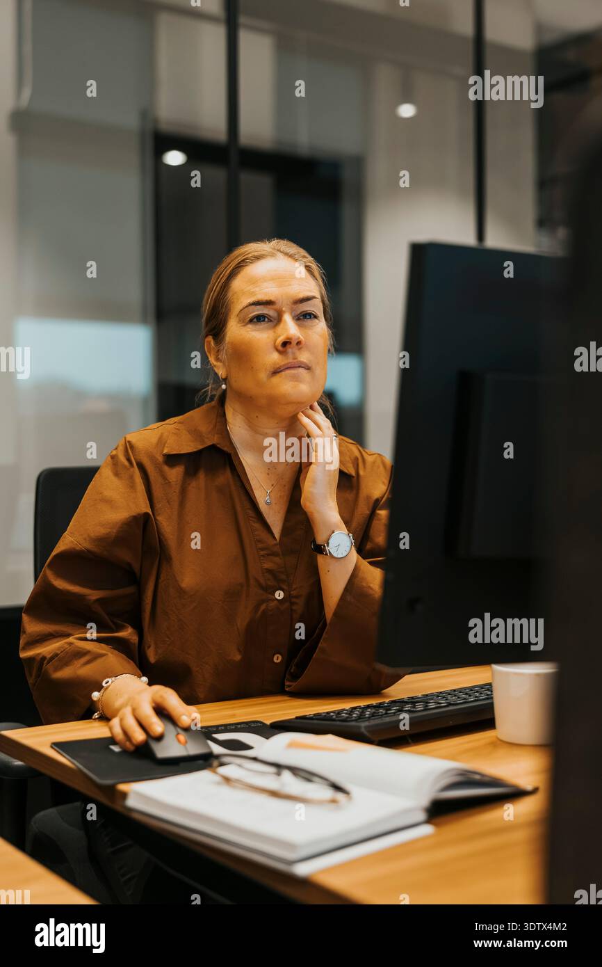 Thoughtful mature businesswoman working on computer while sitting at desk in modern office Stock Photo