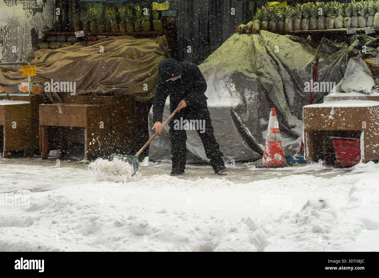 A person clears snow off the sidewalk amid a nor'easter with blizzard ...