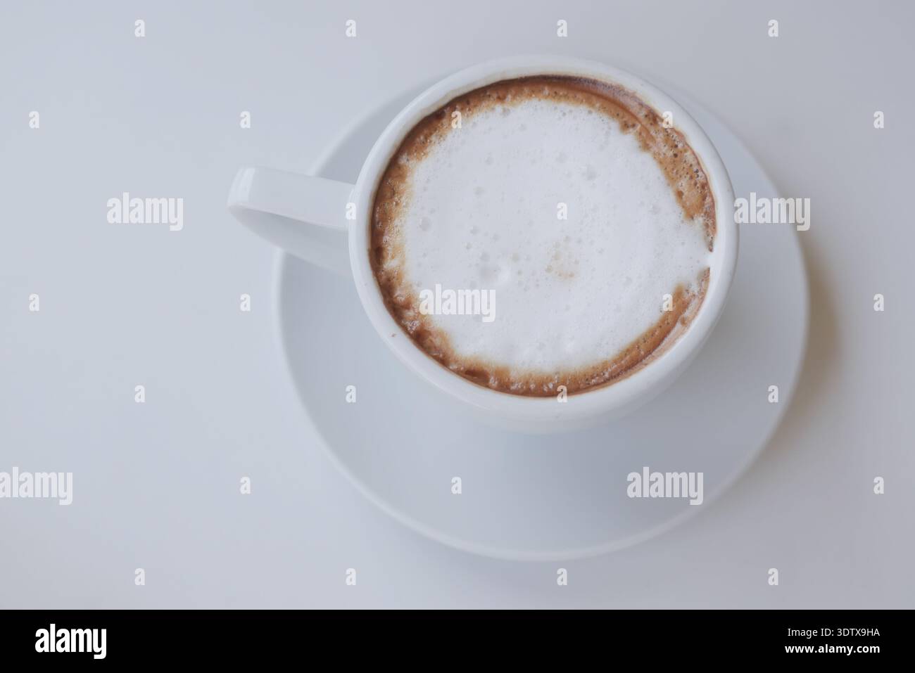 Coffee sits in a white cup on a plain table Stock Photo