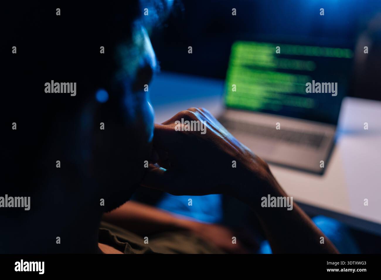 Pensive developer writing code late at night, working on programming software, debugging system issues, ensuring cyber security protection during dark Stock Photo