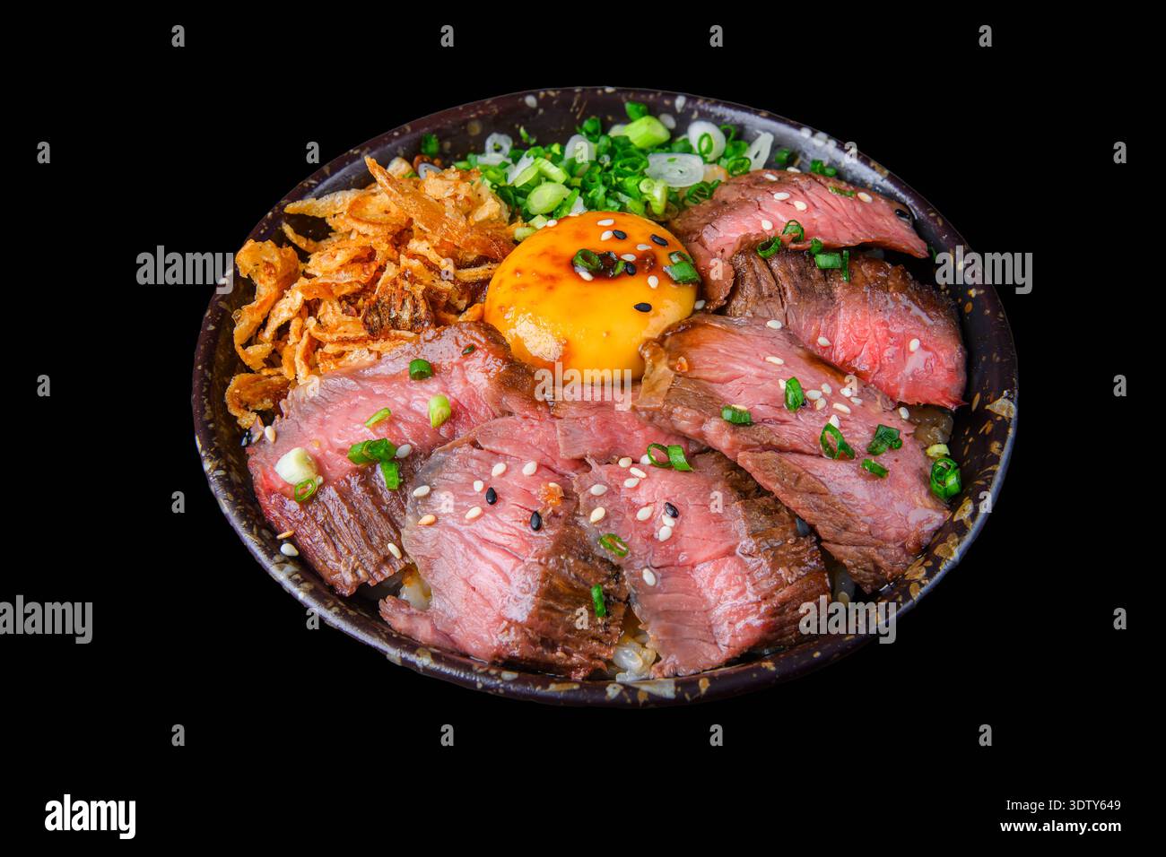 Grilled beef slices served on a rice bowl, topped with raw egg yolk and kimchi, offering a rich and flavorful Japanese dish. Isolated on a black background Stock Photo