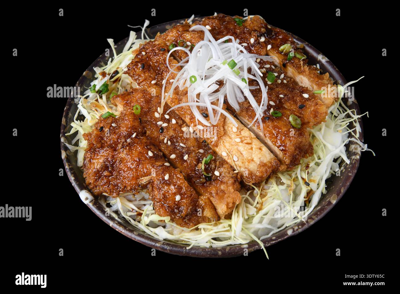 A bowl of crispy fried chicken pieces coated in savory sauce, served over steamed rice and garnished with shredded scallions. Stock Photo