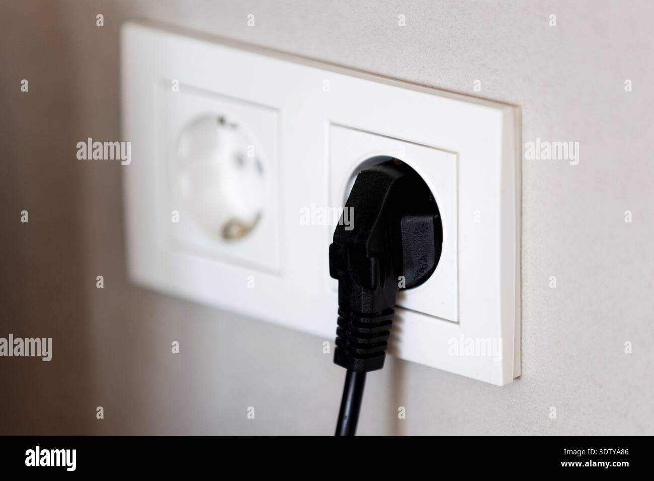 Black power plug connected to white wall socket, home electricity concept Stock Photo