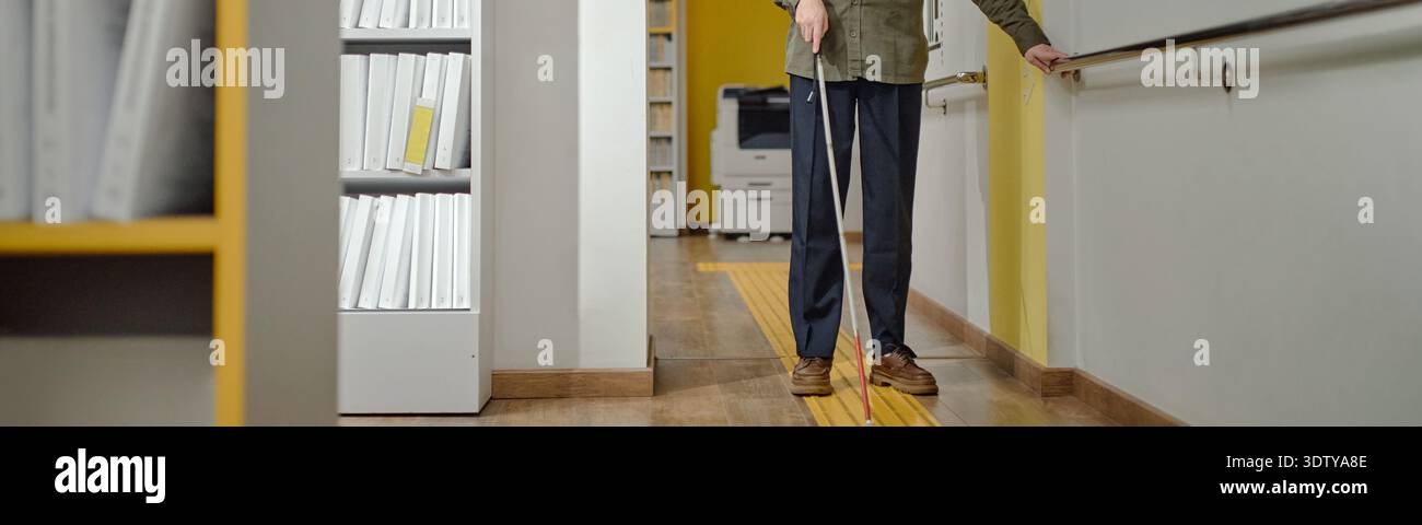 Blind Man Navigating Library Hallway Using Cane and Guide Rail Stock Photo