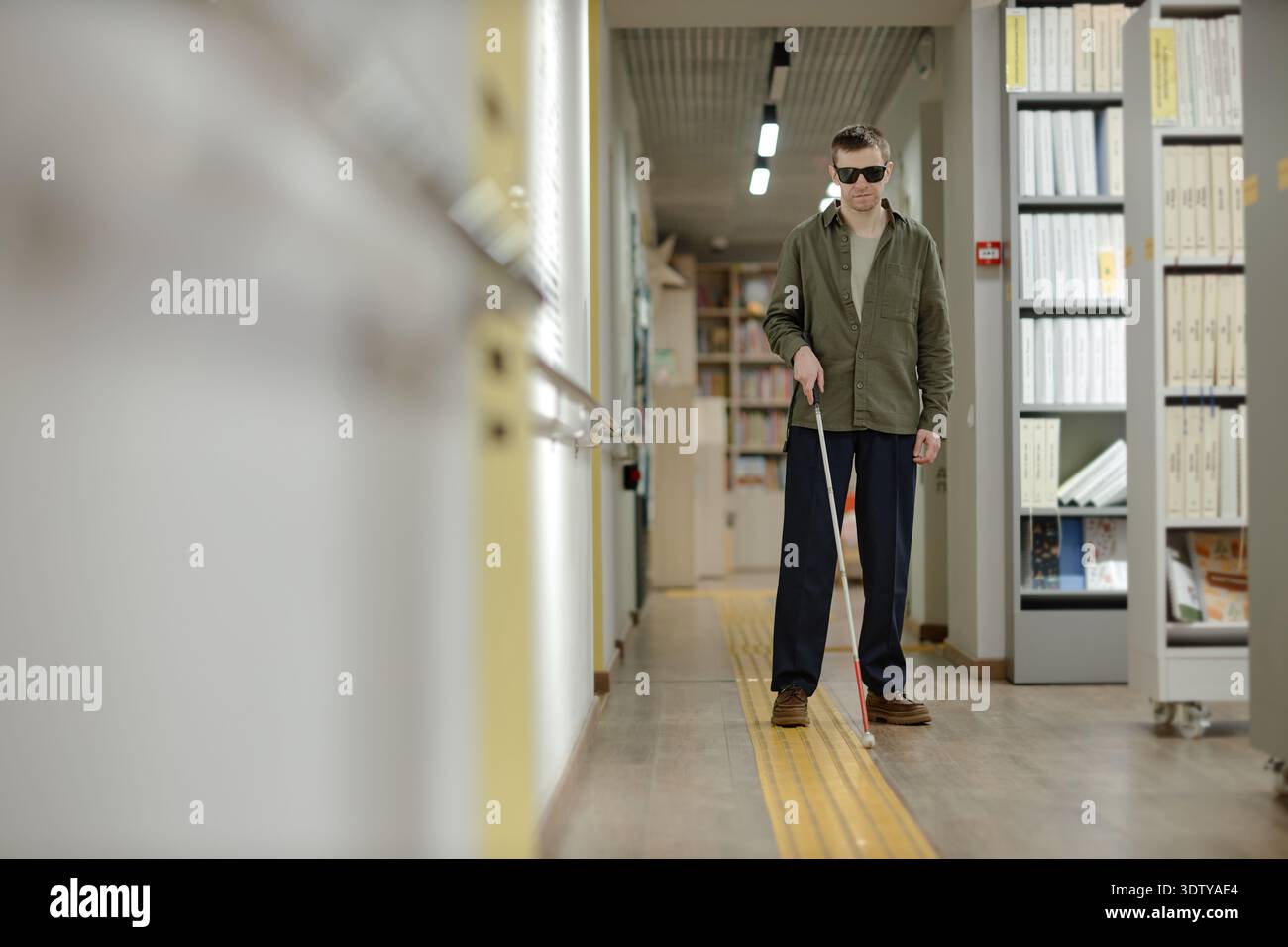 Young Adult Man Navigating Library Corridor Using Cane Independently Stock Photo