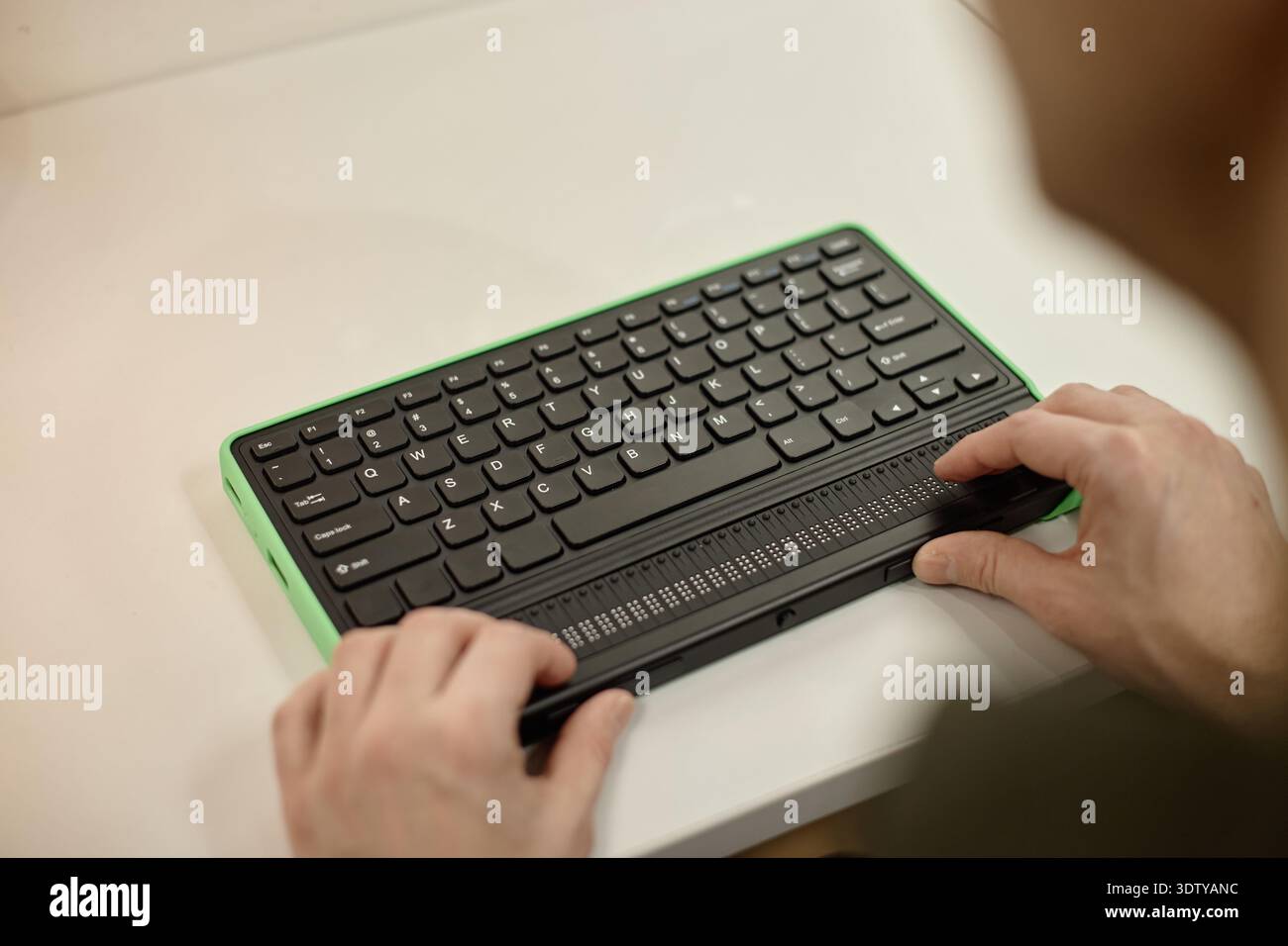 Young Adult Man Using Braille Display Keyboard in Library Setting Stock Photo