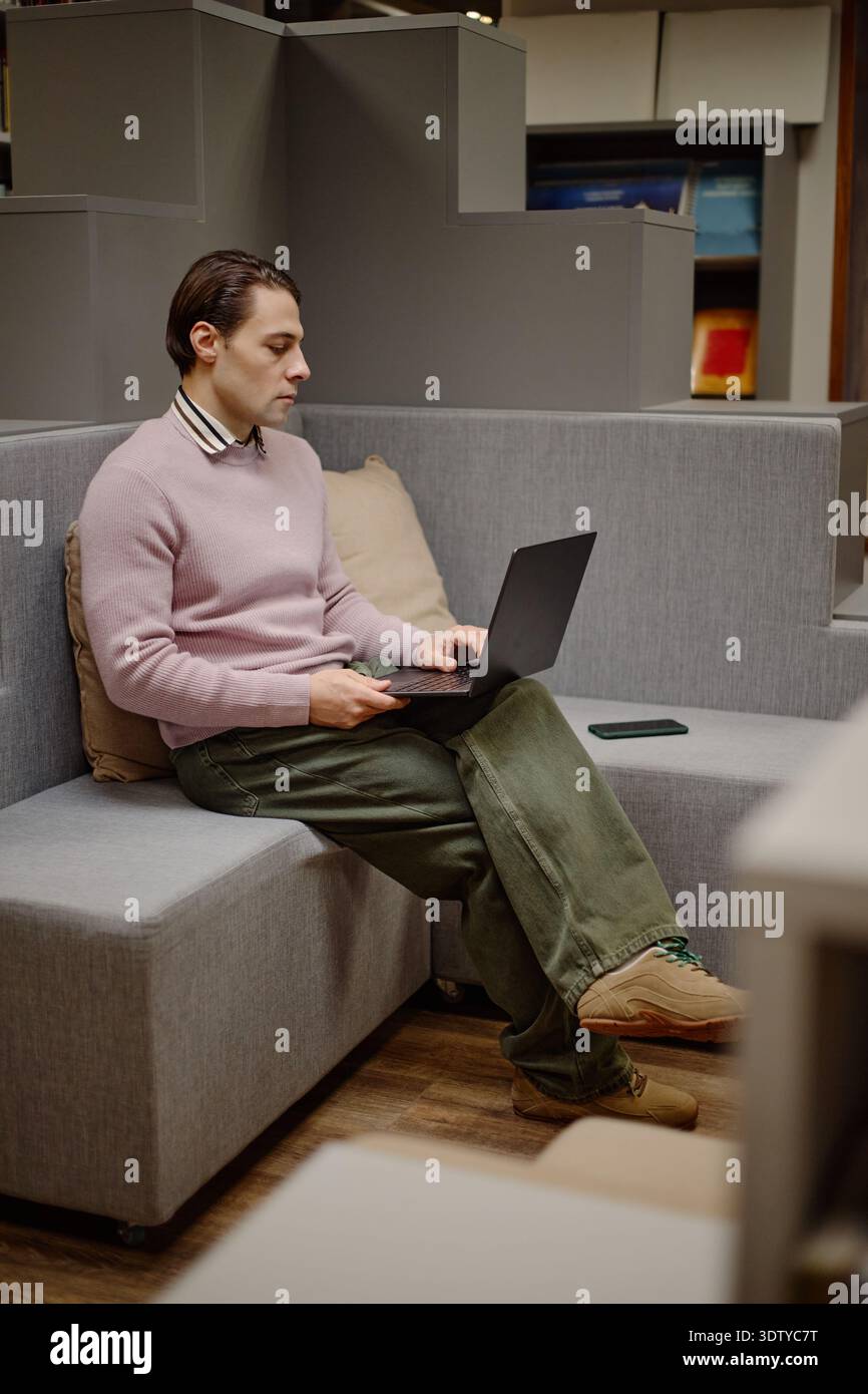 Young Man Using Laptop While Sitting in Library Reading Area Stock Photo