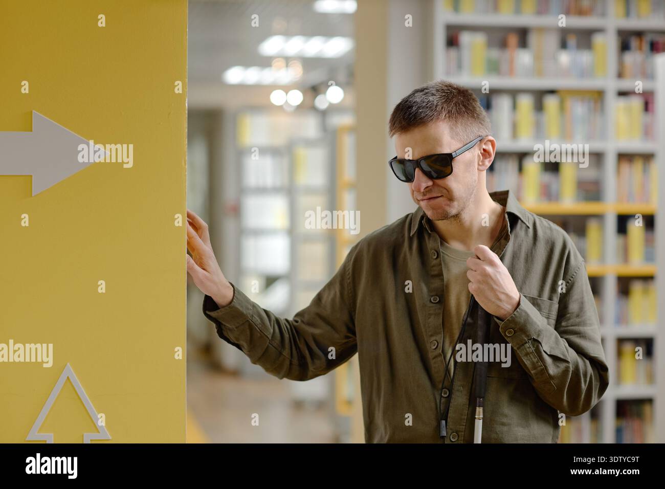 Young Adult Man Navigating Library Using Cane While Blind Stock Photo