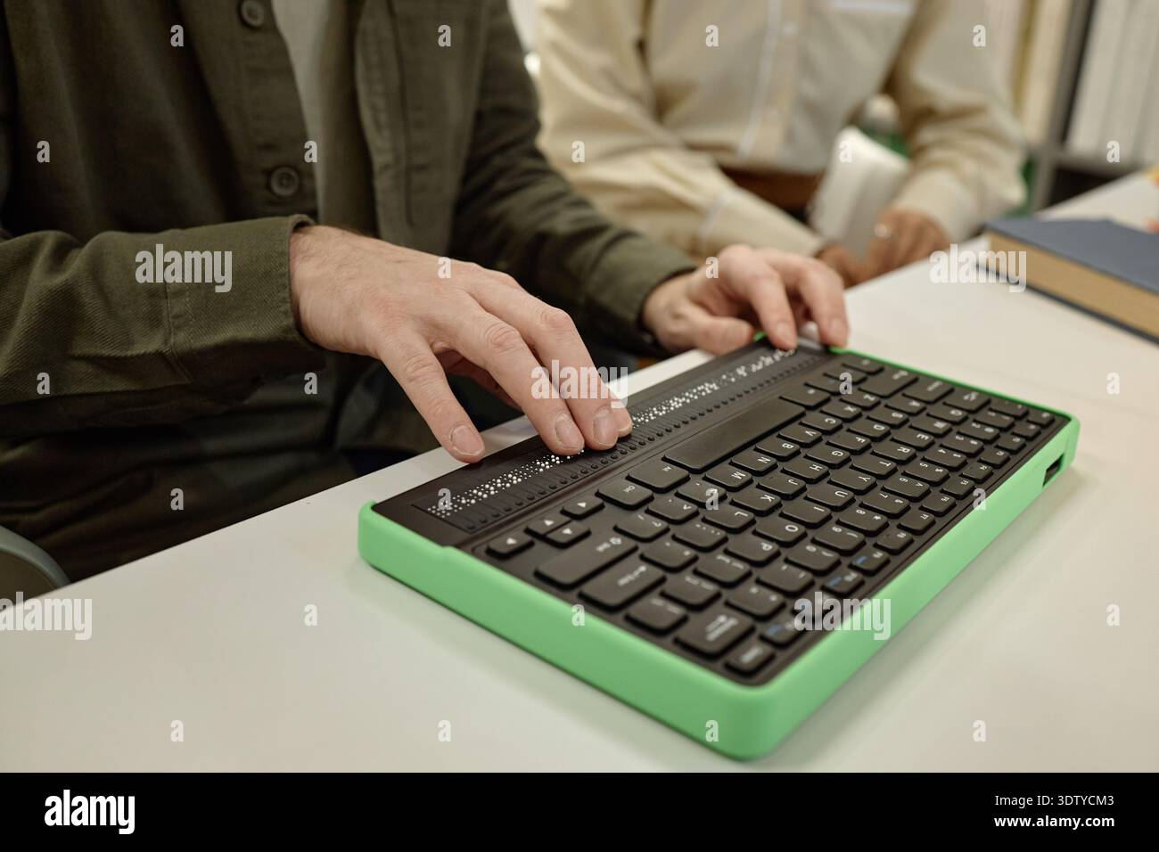 Young Man Using Braille Keyboard While Reading Book in Library Stock Photo