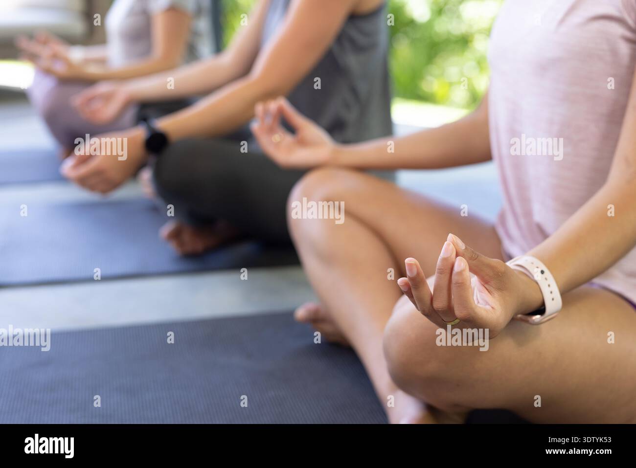Three adult females practicing yoga in studio on dark mats showing Gyan mudra wearing athletic tops Stock Photo