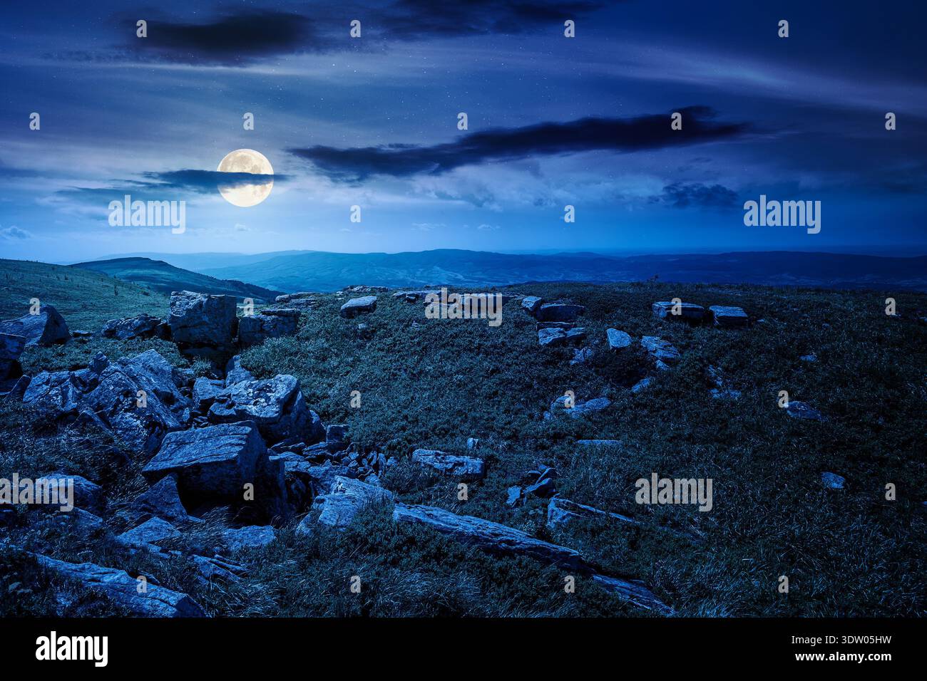grassy alpine meadow in carpathian mountain landscape at night. sharp rocks and huge boulders among lush grass on rolling hills in full moon light. op Stock Photo