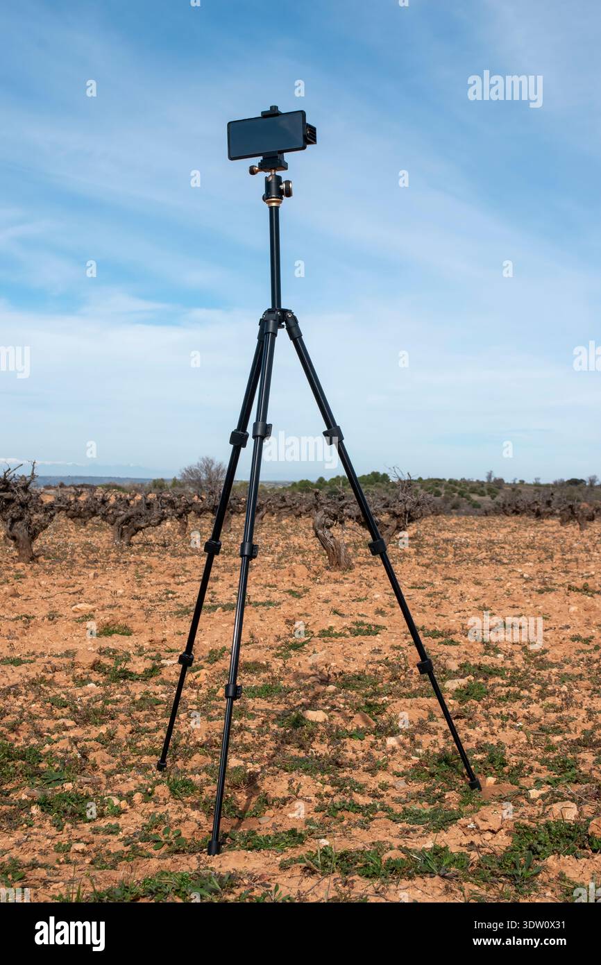 Smartphone en trípode capturando video en un campo rural bajo un cielo despejado. Stock Photo