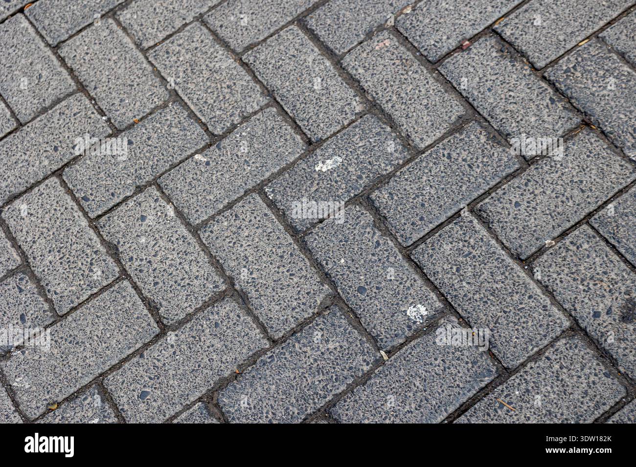 Gray textured interlocking brick pavers forming a classic herringbone pattern, creating a durable and decorative surface for pathways, sidewalks, and Stock Photo