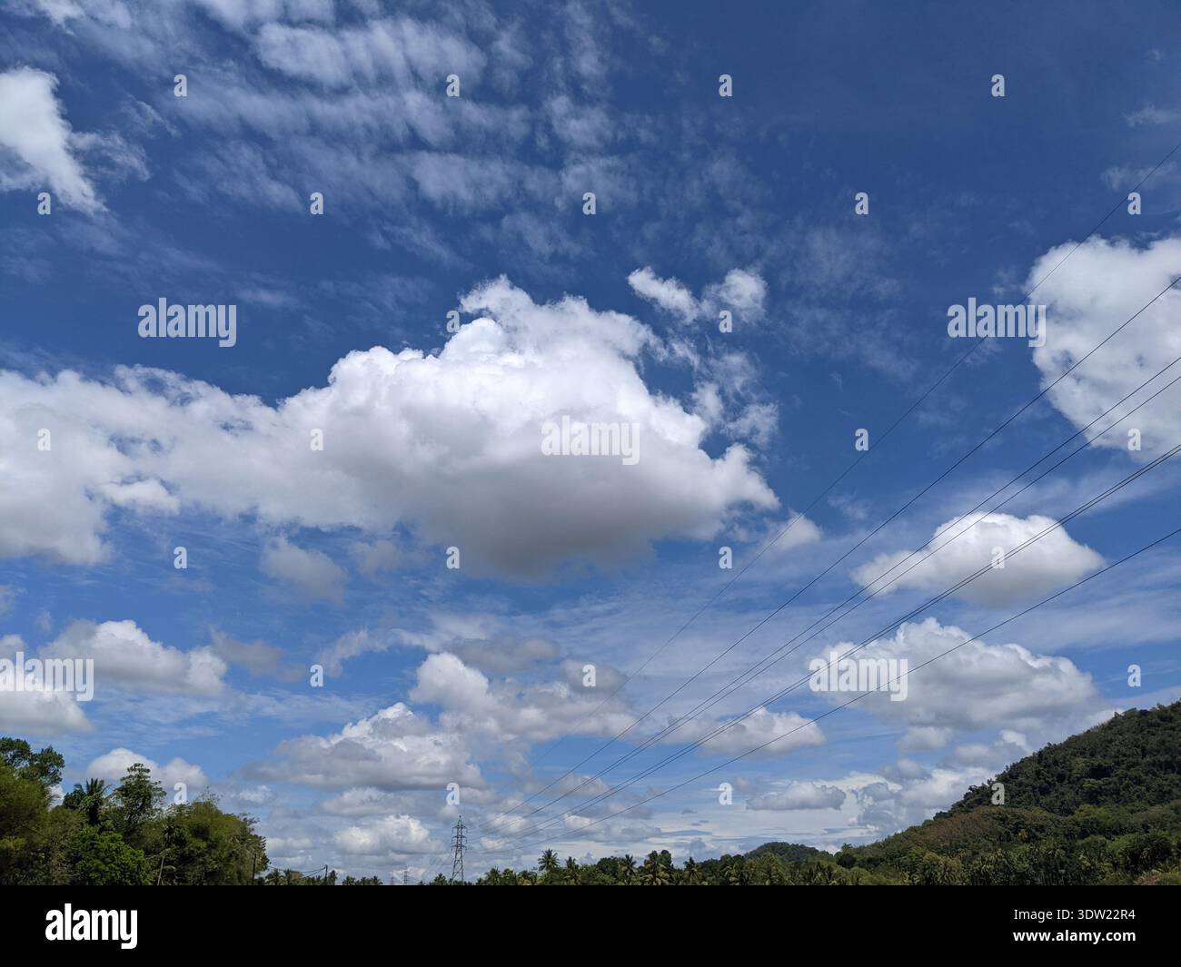 Beautiful white fluffy clouds in a bright blue sky over a rural landscape in Alawwa, Sri Lanka - Smartphone Captured Stock Image