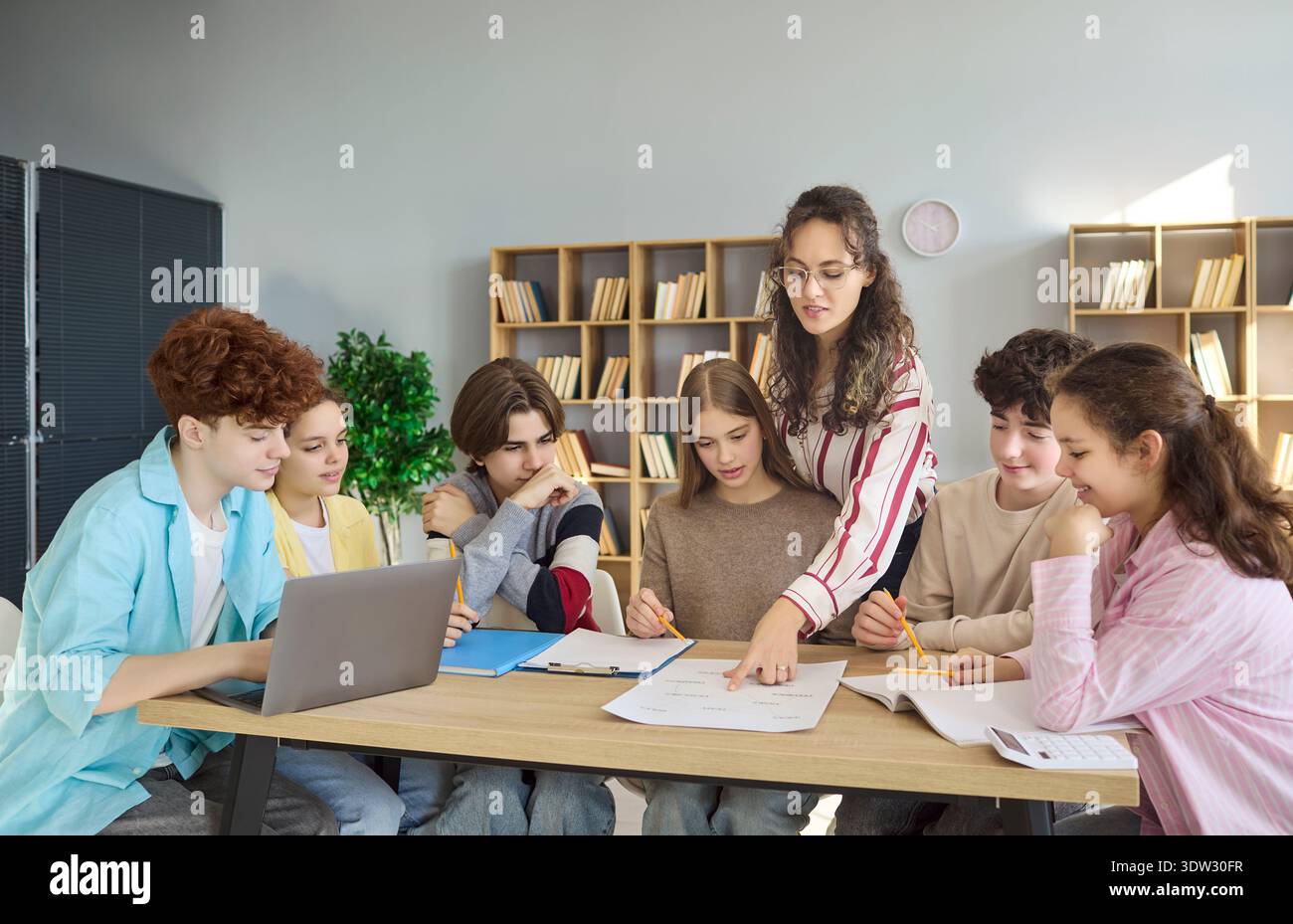 High school students and teacher collaborating on project in classroom library Stock Photo