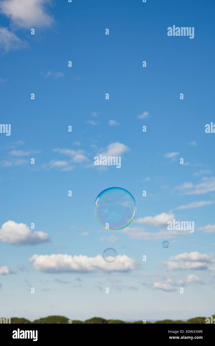 Rainbow-colored soap bubble floating against a beautiful blue sky with white clouds. Stock Photo