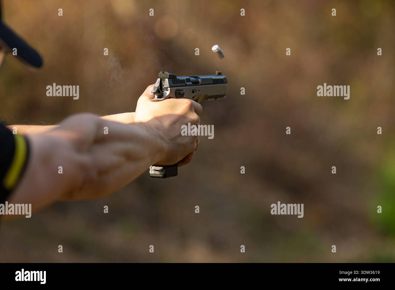 Close-up of hands firing a handgun with a flying shell casing and smoke ...