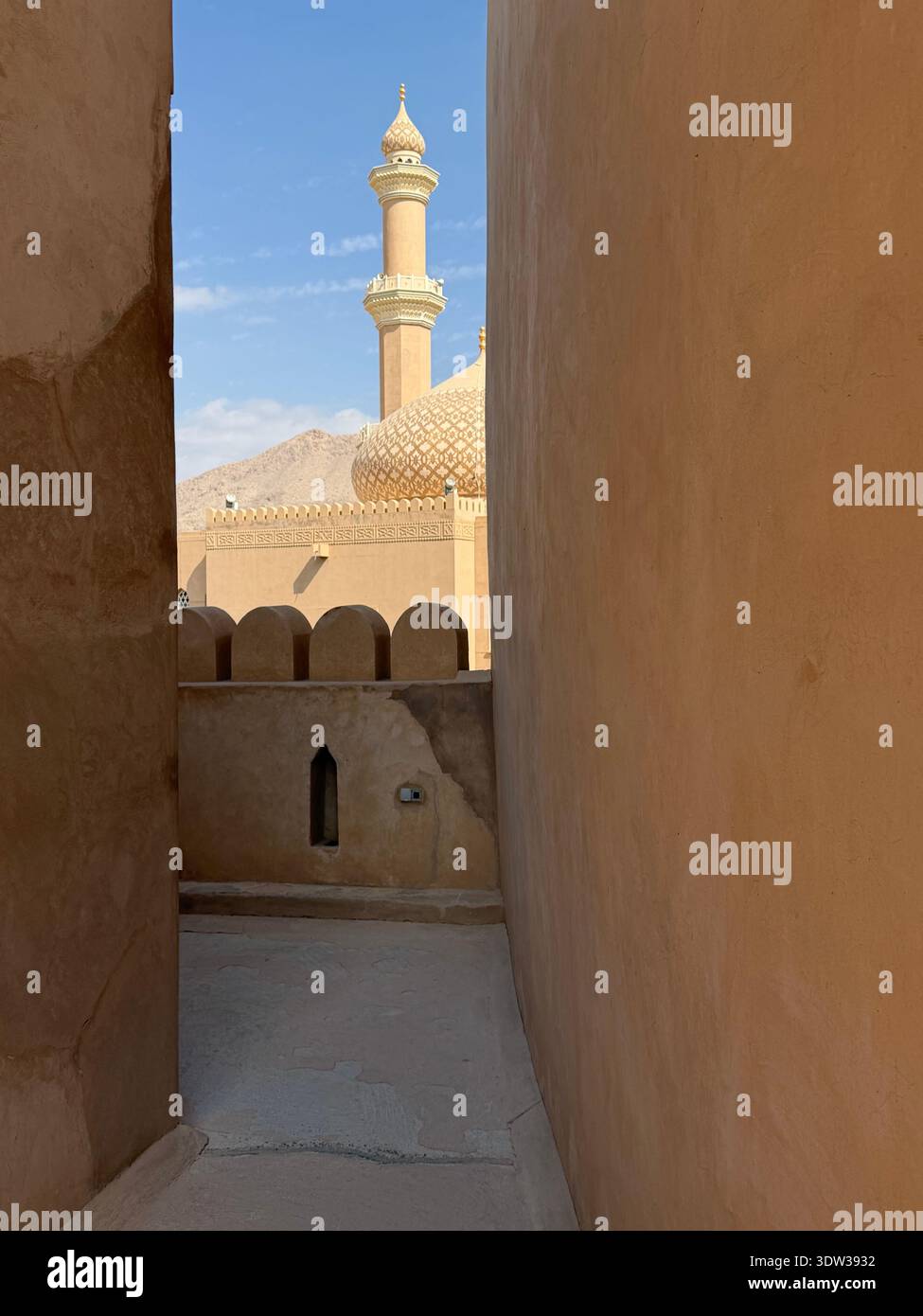 View of mosque minaret and dome framed by traditional adobe walls in Nizwa, Oman, highlighting Islamic architecture and historic desert town setting. - Smartphone Captured Stock Image