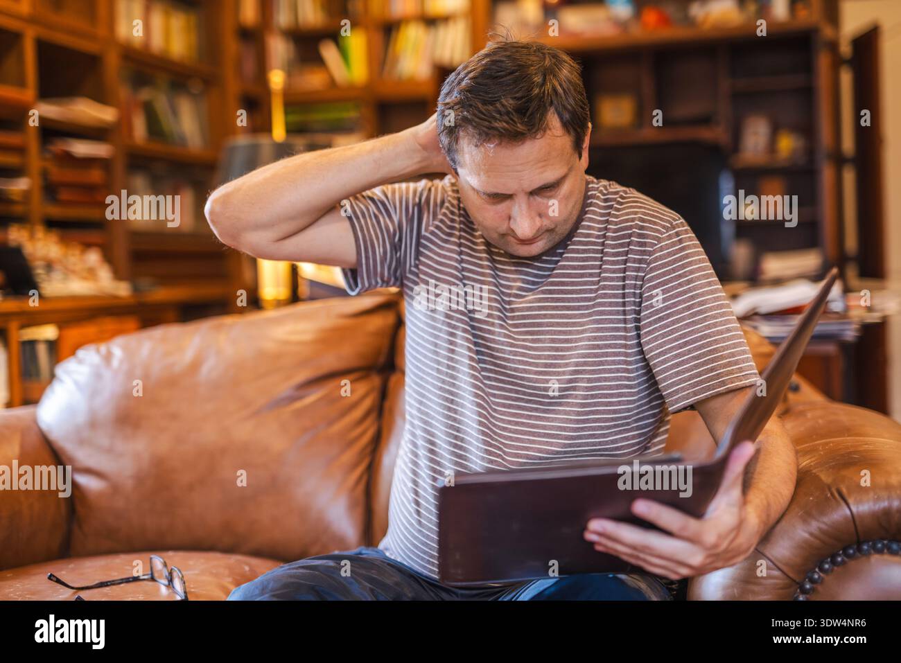 Man reviewing documents with worried expression while sitting on sofa at home Stock Photo