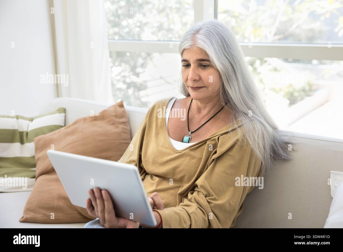 Pretty aged Hispanic woman sitting on couch with digital tablet Stock Photo