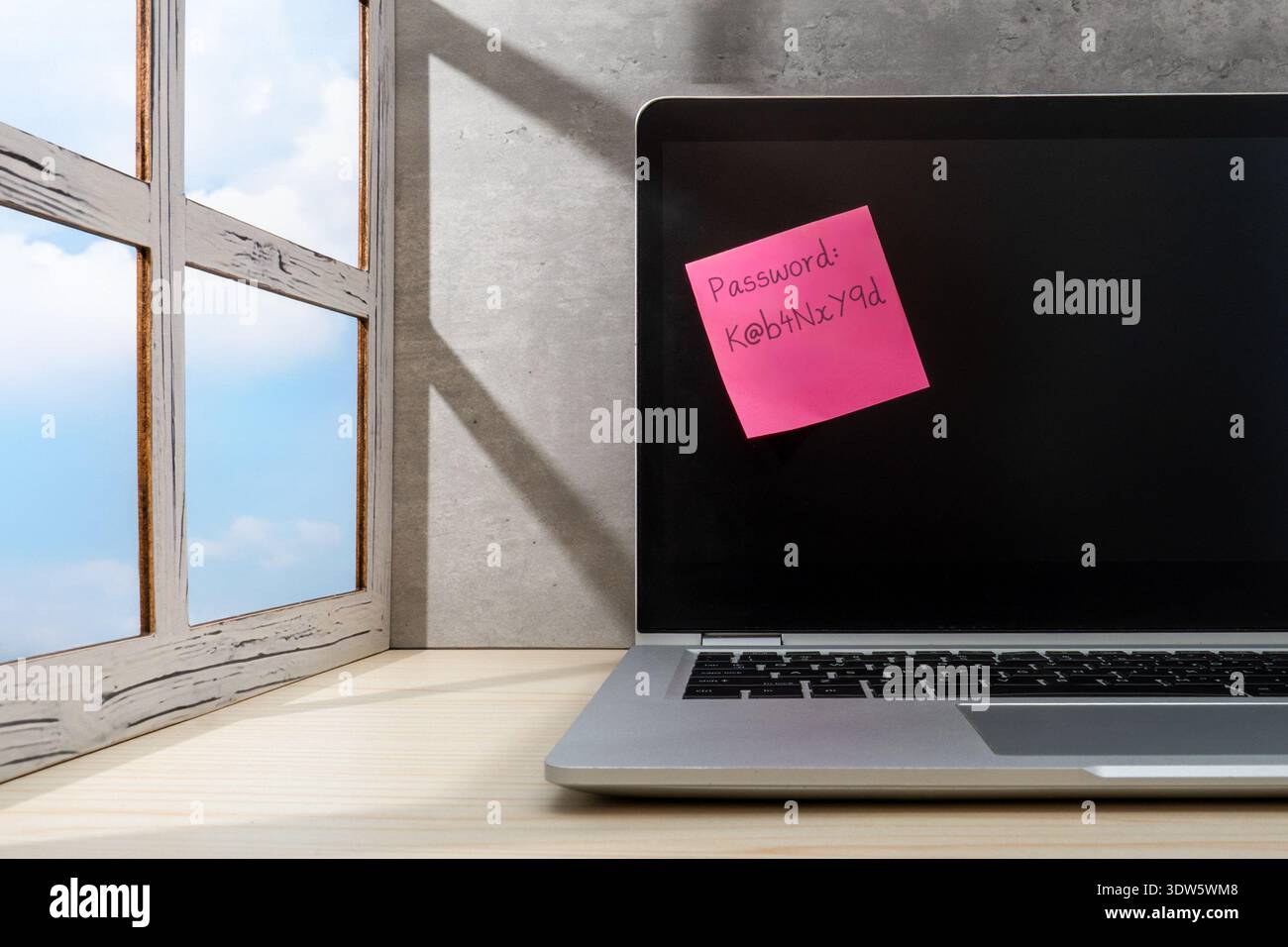 A note with a complex password written on it is attached to a laptop screen. Cybersecurity, data privacy risks, password management concept. Stock Photo