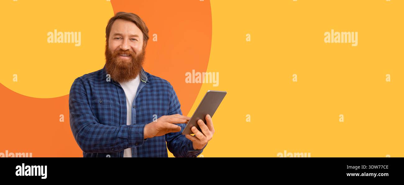 Man Using Tablet Standing Against Bright Yellow Background With Simple Design Patterns Stock Photo