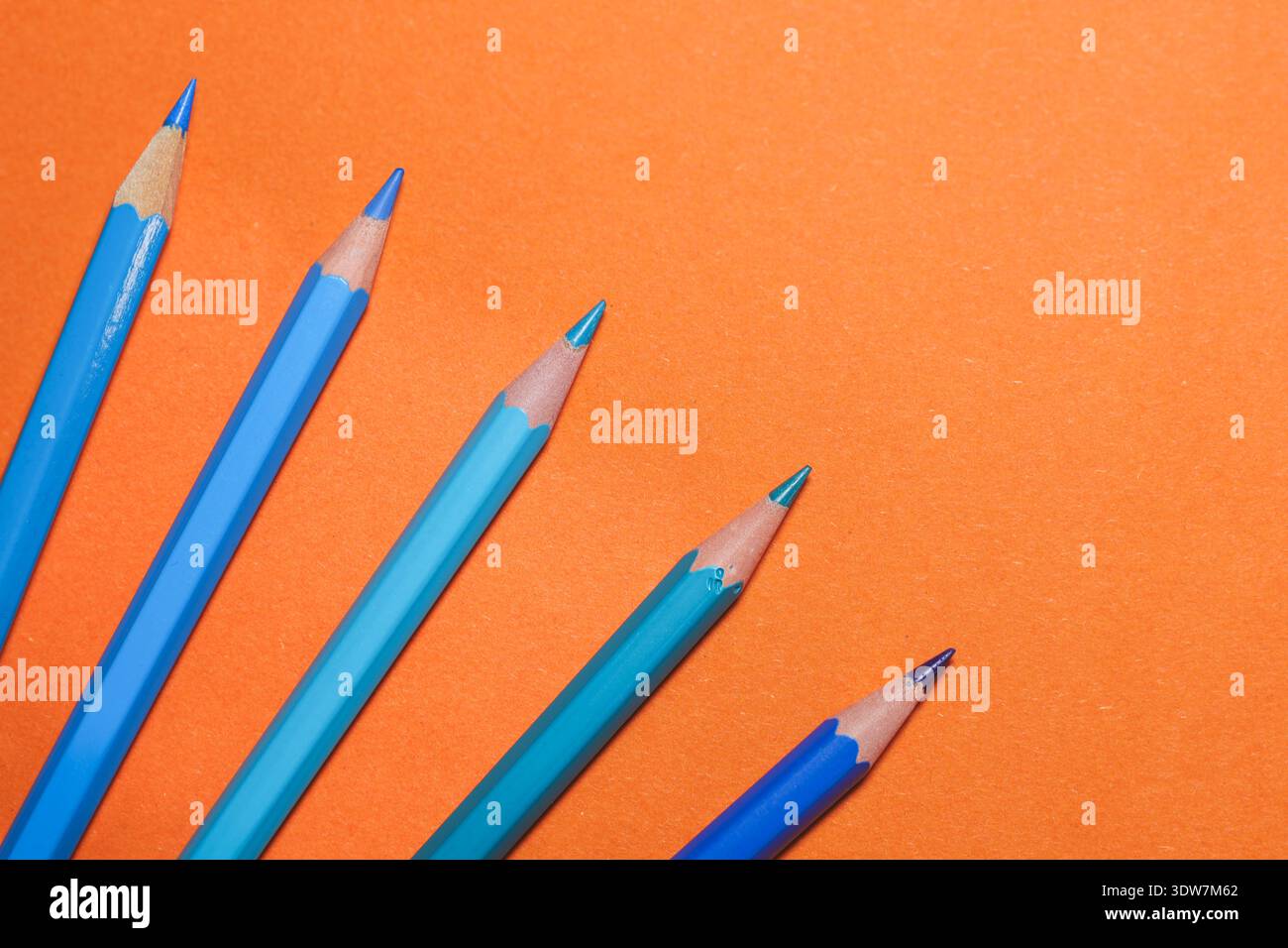 blue and orange pencils arranged in dynamic diagonal lines over a bold orange surface, illustrating complementary colour contrast Stock Photo