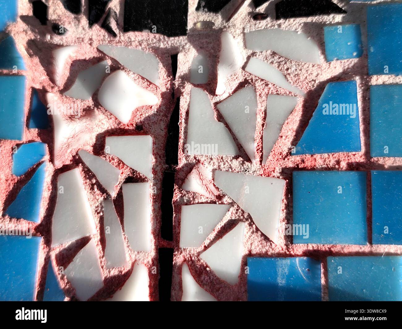 Close-up of a colorful mosaic made of blue, white, and black ceramic tiles with visible cracks and pink grout texture in sunlight Stock Photo