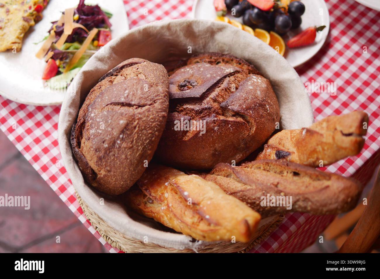 Fresh bread in a wicker basket on a checkered tablecloth Stock Photo