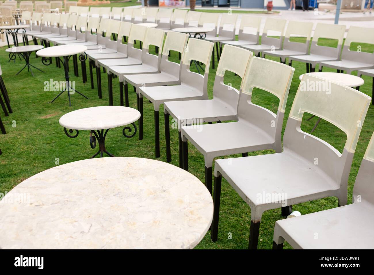 Rows of gray plastic chairs and round tables arranged on green grass in an outdoor setting, ideal for events or gatherings Stock Photo
